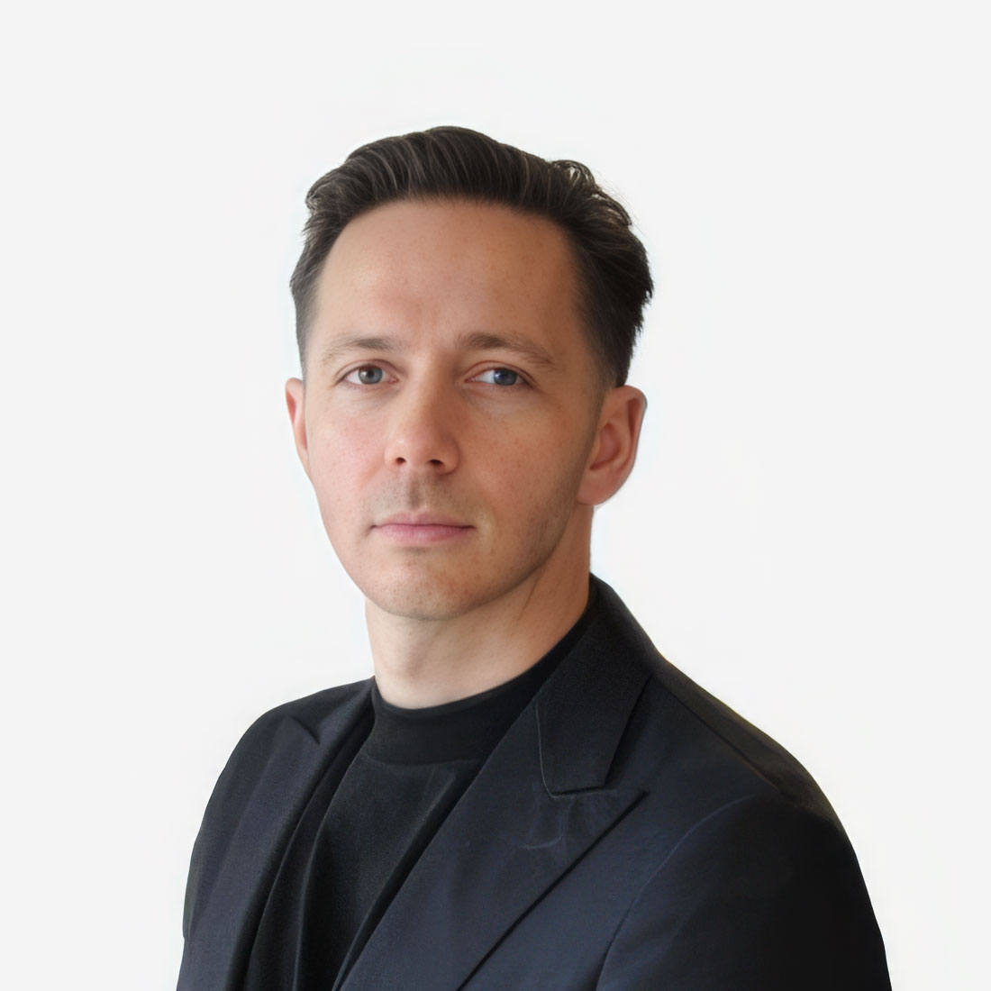 Professional headshot of a man with short dark hair wearing a black blazer against a white background, looking at the camera.